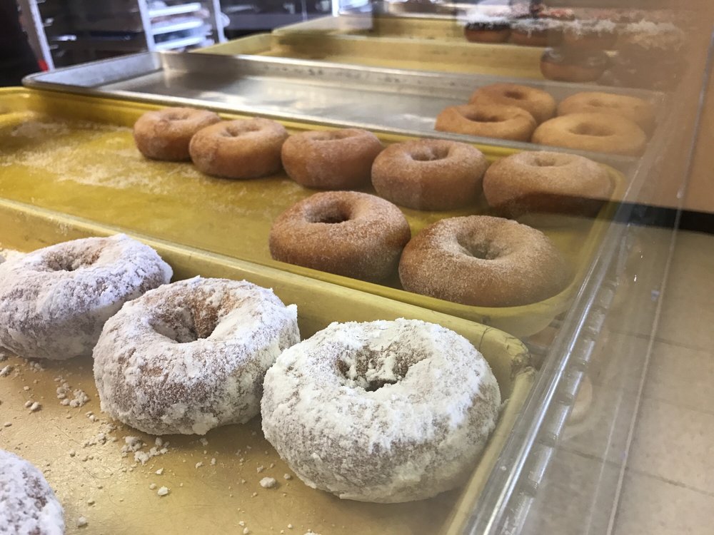 Five kinds of donuts on display in the glass display case. The one closest to the case is powdered sugar.