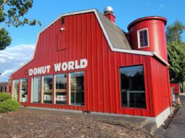 The outside of Donut World. It looks like a red barn with metal siding and large windows.