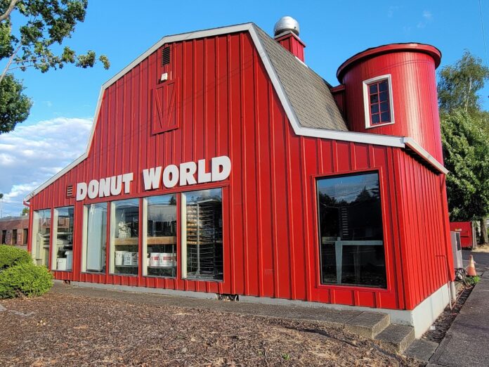 The outside of Donut World. It looks like a red barn with metal siding and large windows.