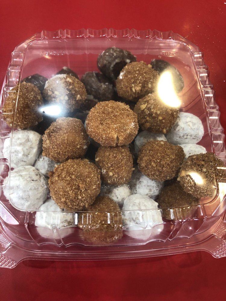 A clear plastic container with a lid full of donut holes. There appears to be three kinds inside the box: cinnamon, powdered sugar, and chocolate.