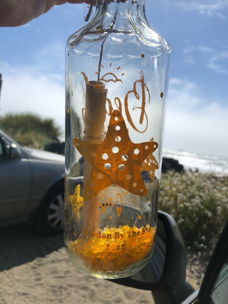 A clear bottle with a dark yellow painted starfish on it, and a rolled up scroll inside in Bandon, Oregon.  It's part of the 'message in a bottle' event.
