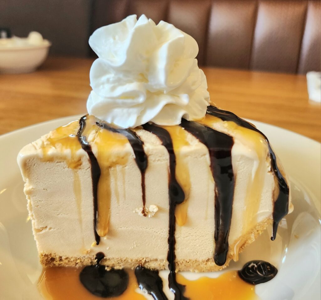 A piece of pie with chocolate and caramel drizzled over the top and down the sides. It has a dollop of whip cream on top.