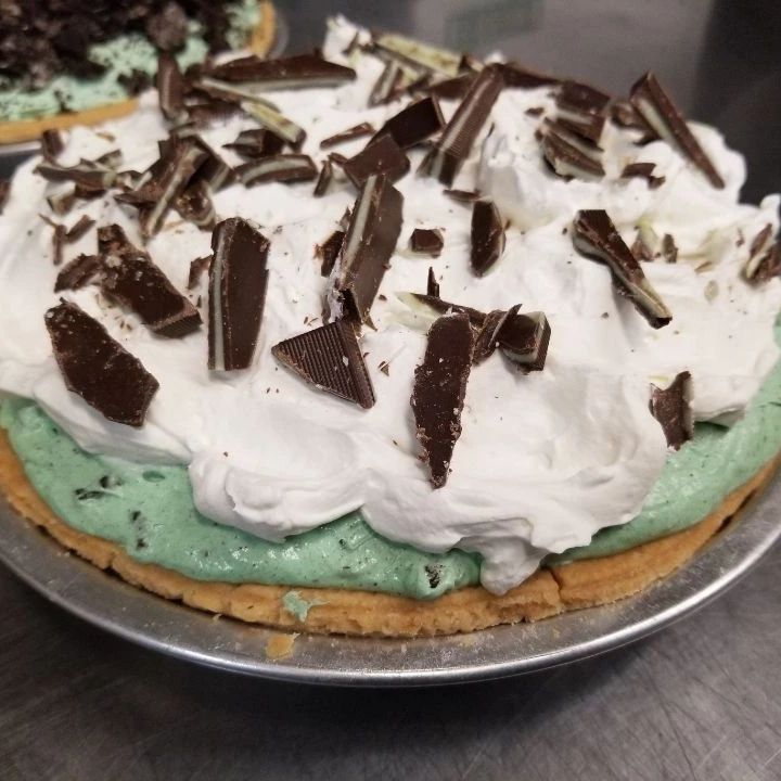 A green pie with whip cream and mint chocolate candy pieces scattered on top. It looks tasty.
