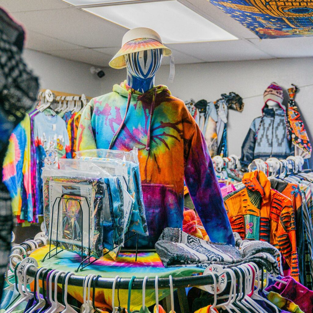 A display with a colorfully tie dyed hoodie, several hats, and other cute garments in the background.