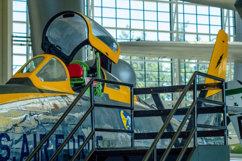 An F-84 cockpit at the Evergreen Aviation And Space Museum. It's silver with dark yellow paint and stairs leading up to it.