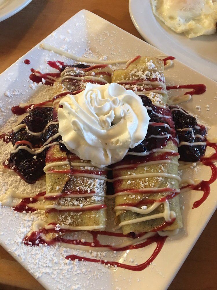 Marionberry Crepes drizzled in red and white sauce with whip cream on top and berries on the side.