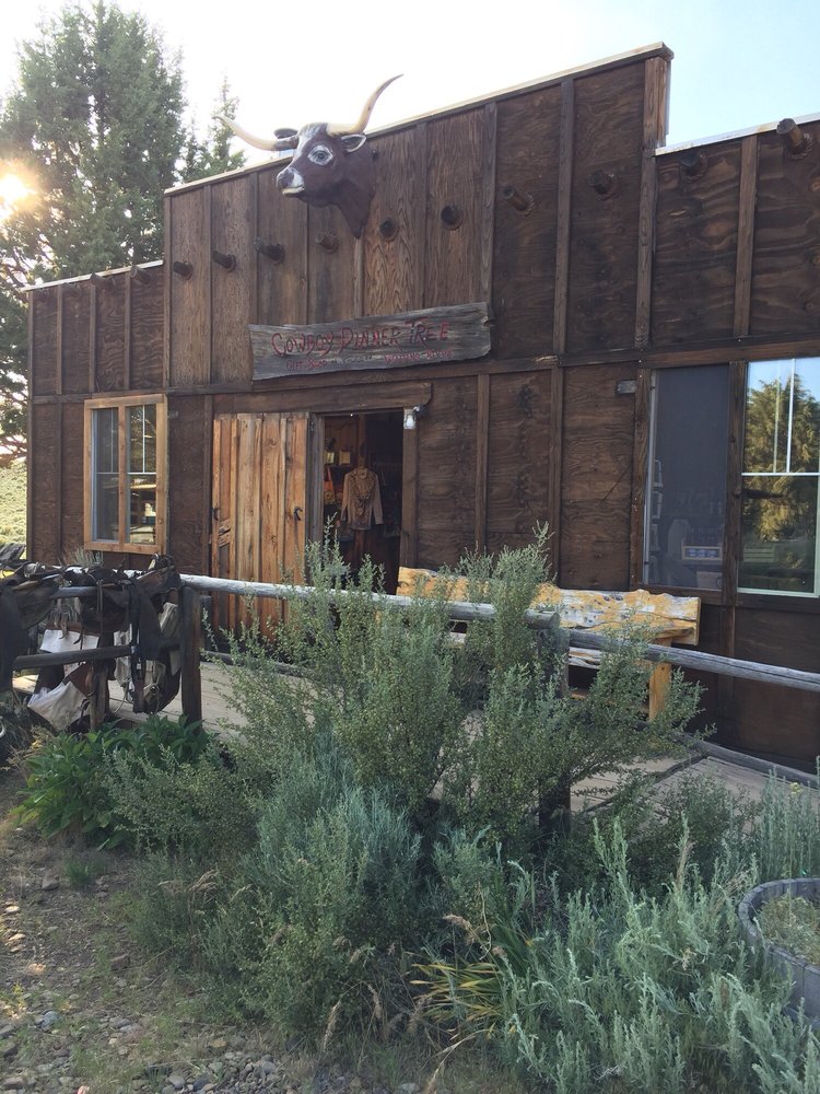 The outside of The Cowboy Dinner Tree. It's a rustic wood building with sage brush outside and saddles hanging over a wooden rail.