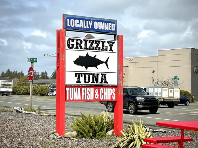 The sign for Grizzly Tuna. The sign is white with black words and a black silhouette of a tuna fish. It says 