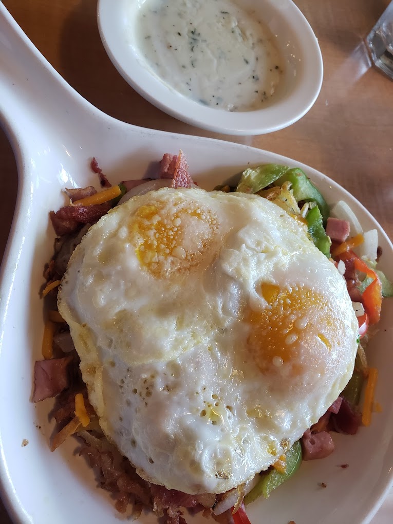 Two fried eggs on top of hash browns with ham and lots of vegetables.