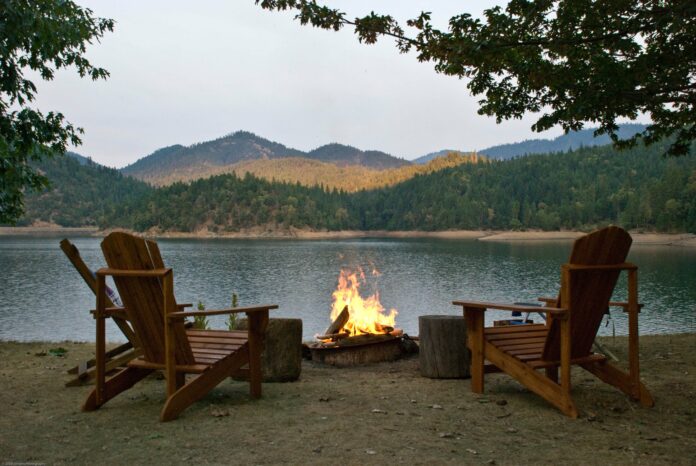 Two chairs and a fire in a fire pit in front of Applegate Lake with mountains in the background.