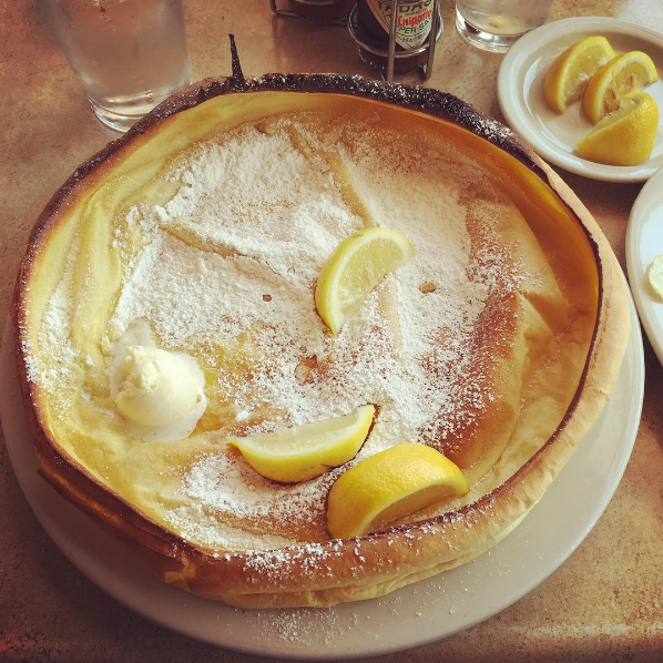 A huge German pancake with lemon wedges, powdered sugar, and butter on top.
