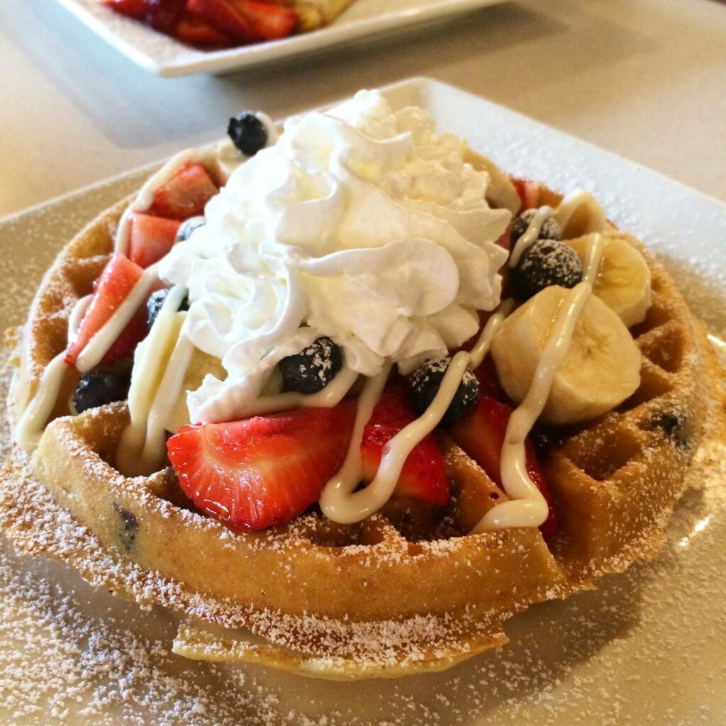 A huge waffle with berries, bananas and whip cream.