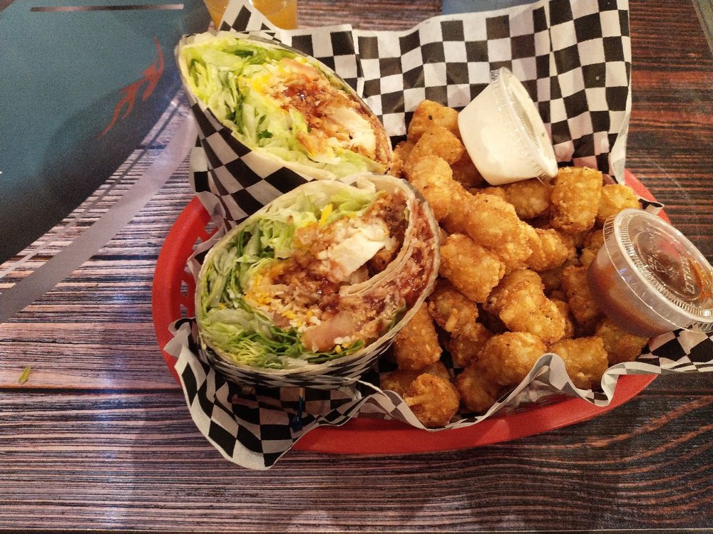 BBQ Chicken Wrap with tater tots. It's in a red plastic basket with a black and white checkered paper food wrapper.