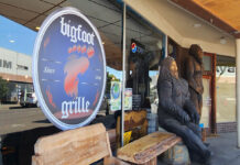 The outside of Bigfoot Grille. There are two huge Bigfoot's carved out of wood out front, and wooden benches to sit on.