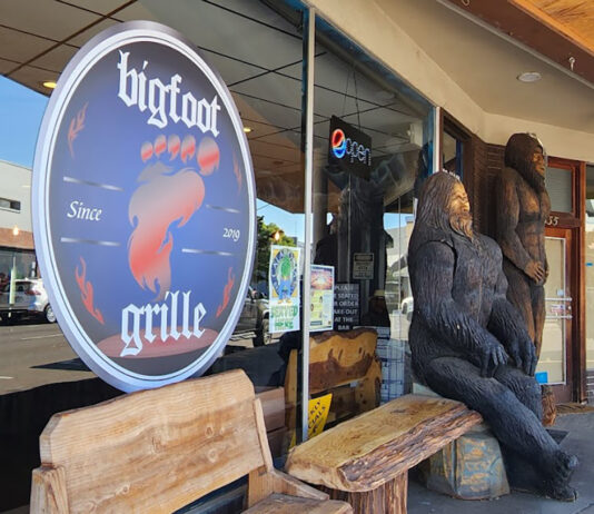 The outside of Bigfoot Grille. There are two huge Bigfoot's carved out of wood out front, and wooden benches to sit on.