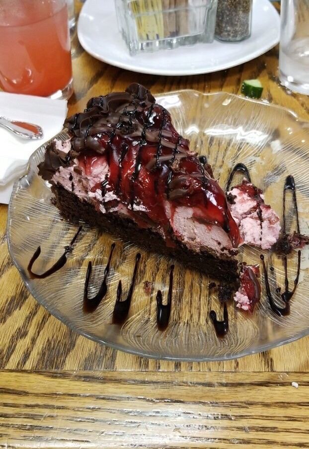 A chocolate cake with pink frosting, red berry topping and a chocolate drizzle. It looks rich and delicious!
