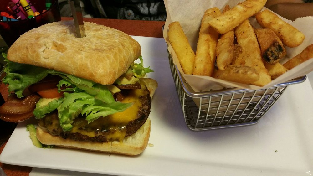 A delicious looking burger with a metal basket of fries.