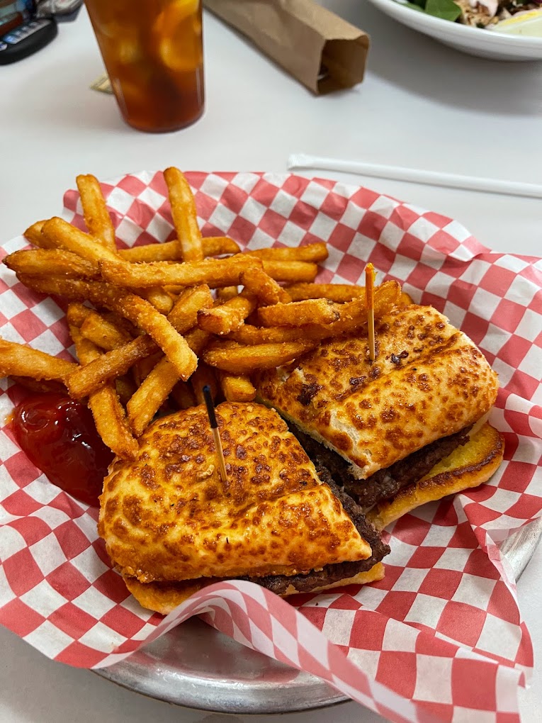 A delicious looking sandwich with a toasted bun, and meat. There are French fries and ketchup next to it. The food is on a plate with a red and white checkered food wrapper.
