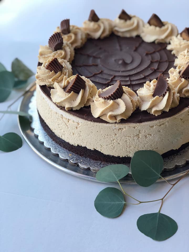 A brown and white cake with peanut butter cup pieces on swirls of frosting. It looks rich and decadent!