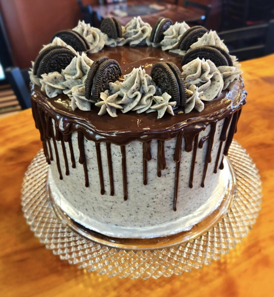 A crazy looking white cake with chocolate drizzled over the top and down the sides. There's frosting piped on top in between Oreo cookies. It looks so good!