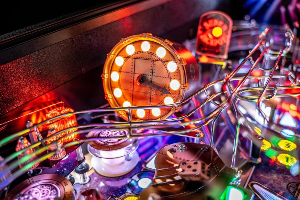 An up close shot of a pinball machine. There's a metal track for a pinball, bright lights, and colorful mechanical parts inside. It looks really cool.
