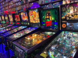 Several brightly lit pinball machines inside Next Level Pinball. The room is kind of dark, so the pinball machines are all lit up brightly. Looks like lots of fun!