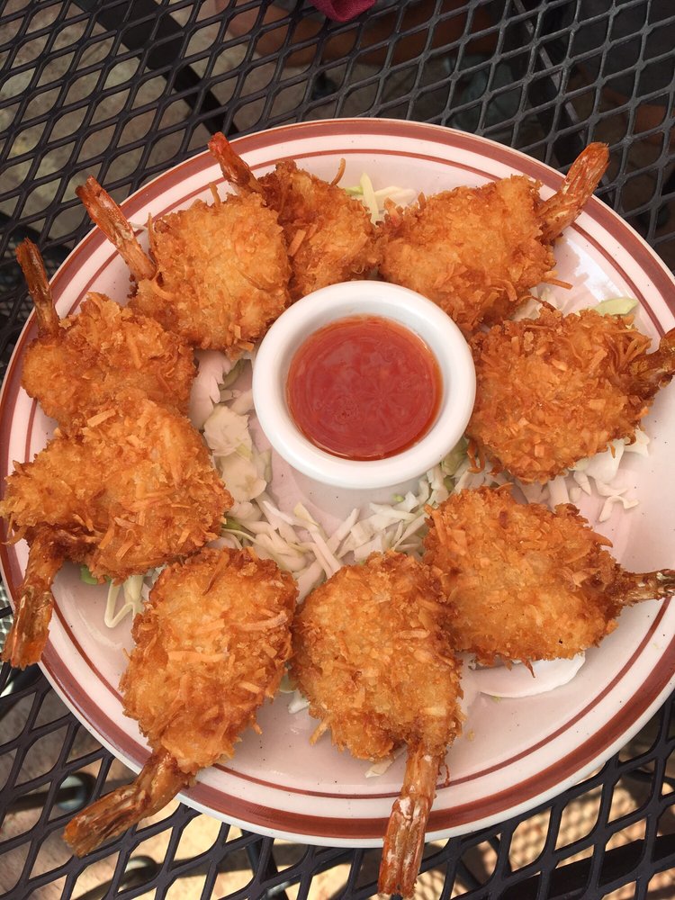 A plate with 9 coconut shrimp in a circle around a small container of red dipping sauce.
