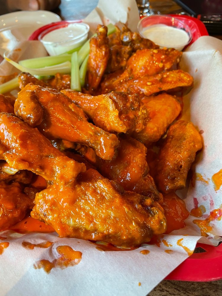 A plate of saucy looking buffalo wings with a container of dipping sauce and celery sticks.