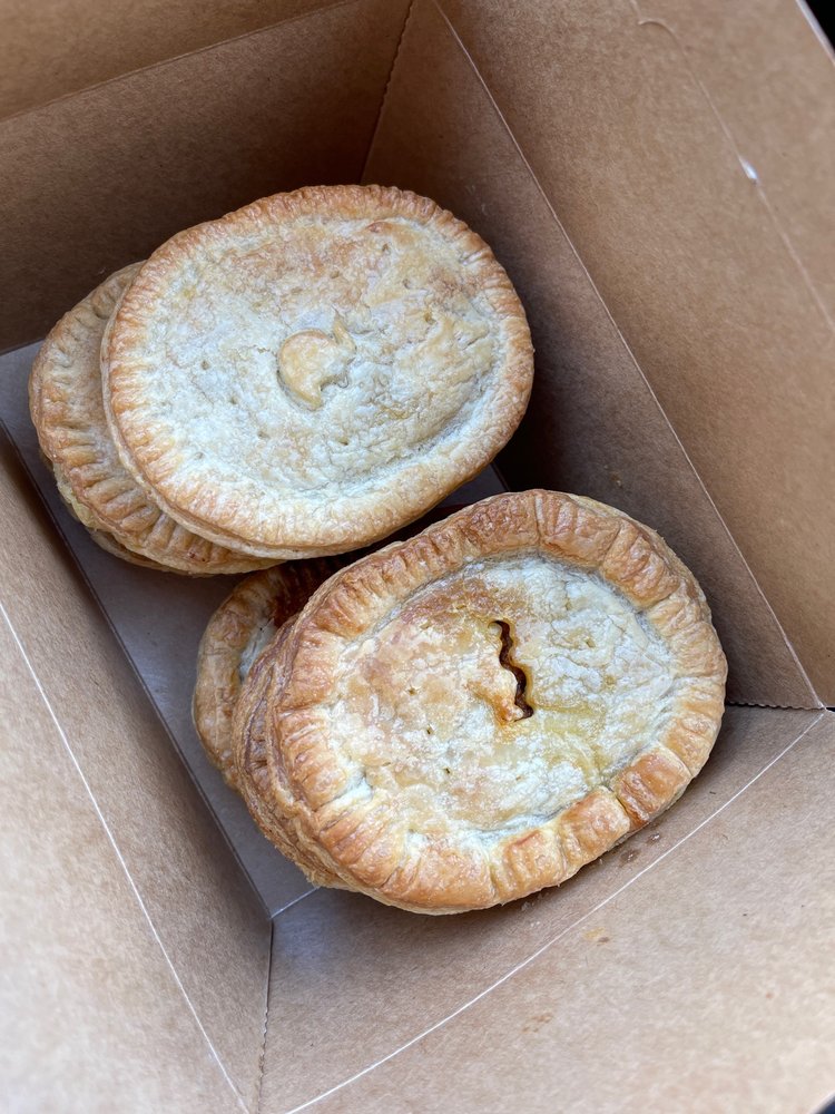 Four meat pies in a cardboard to-go box. The pies are stacked on top of each other.