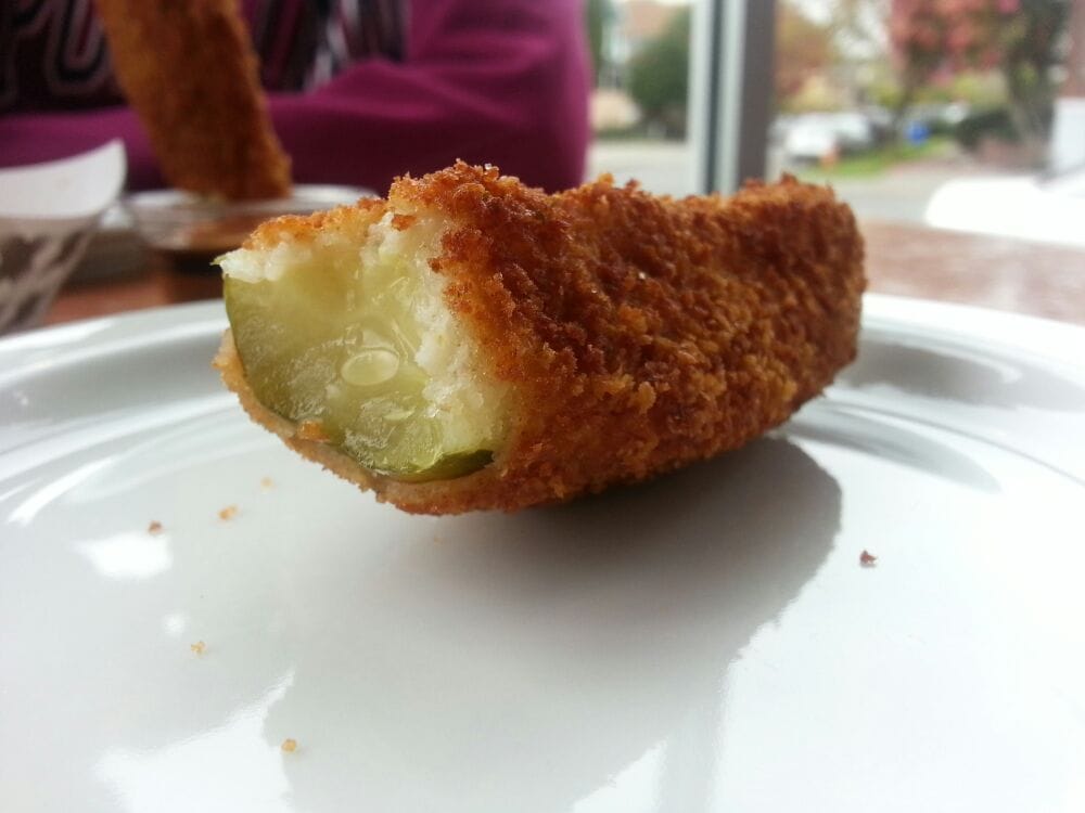 A fried pickle spear with a bite taken out of it. It's crispy and breaded on the outside, and green on the inside.