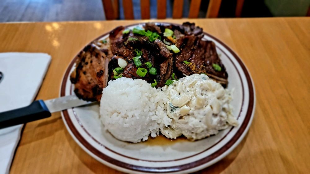 A plate with mac salad, sticky rice and marinated meat with chopped green onion on top.