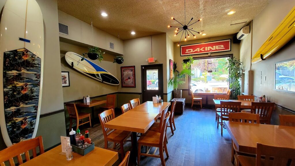 The inside of Noho's. There's a surfboard on the wall, and wooden tables and chairs.