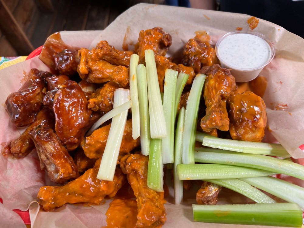 A basket with a variety of chicken wings, celery, and dipping sauces.