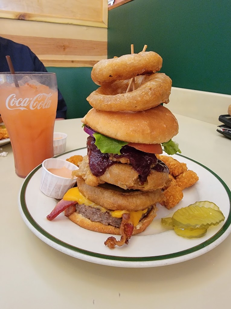 An enormous burger stacked tall with onion rings on the burger and stacked on top of it and held in place by tooth picks.