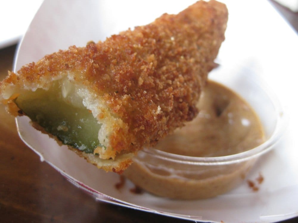 A fried pickle with a bite taken out of it and a container of dipping sauce.