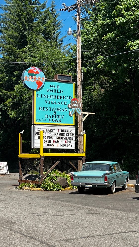 The teal and yellow sign on the side of the highway for Old World Gingerbread Village. There's a classic teal car parked under the sign in the photo.