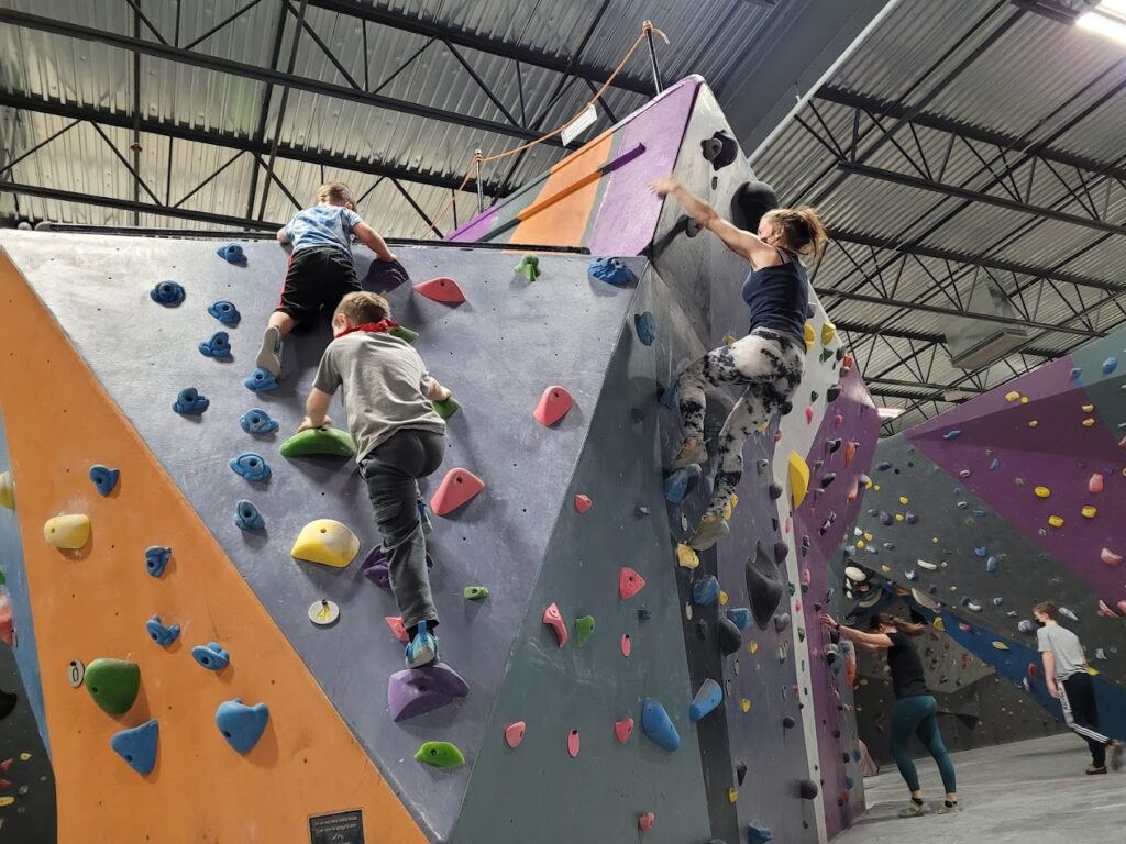 Two kids and several adults climbing up an indoor rock wall.