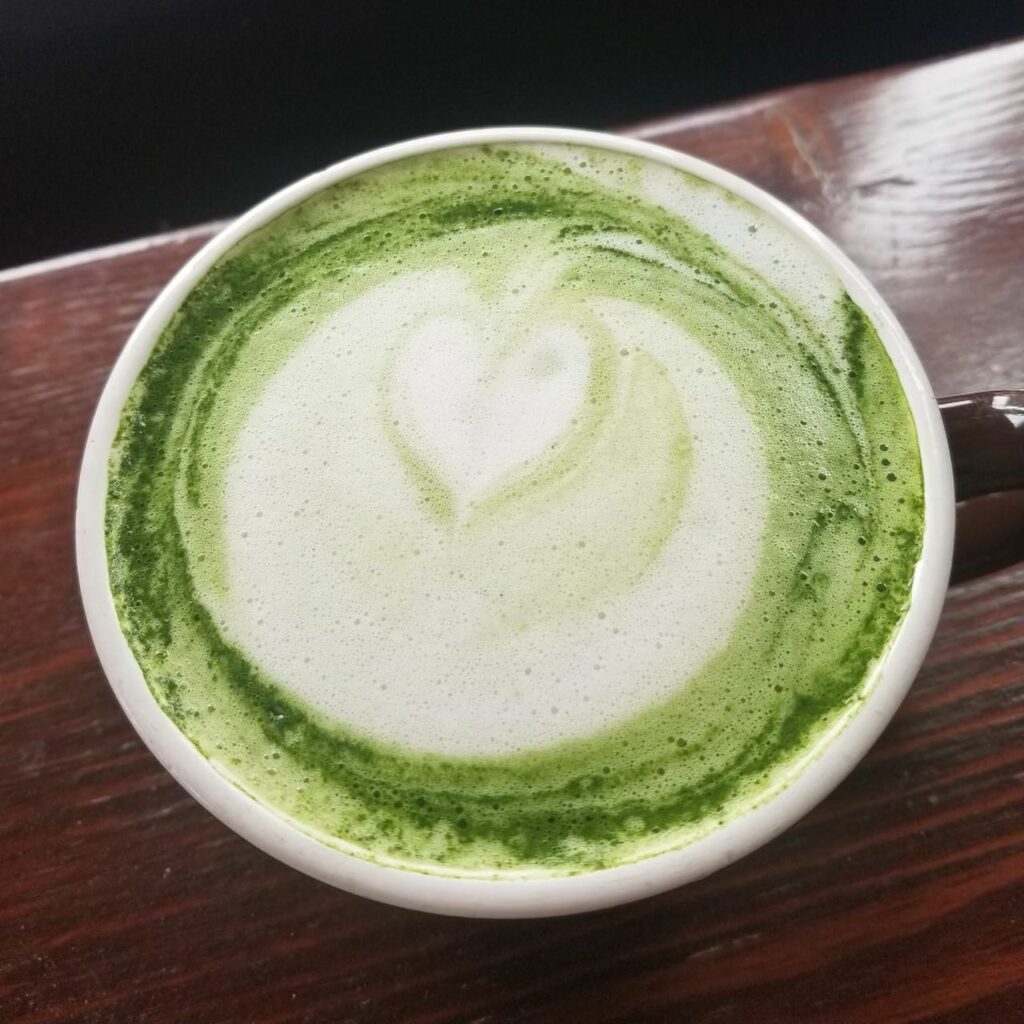 A hot green drink with a foam design on top.