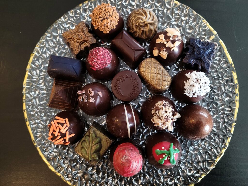 A plate with a variety of colorful truffles and fine chocolates on it.