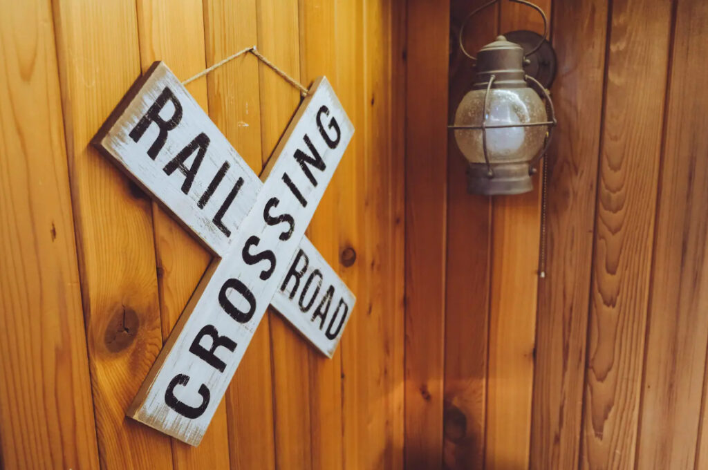 A white Rail Road Crossing sign hanging on a wood panel wall.