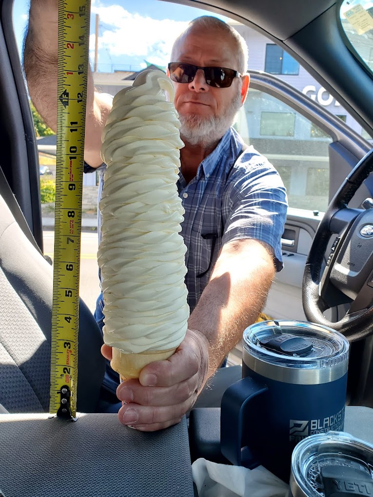 A man holds up an ice cream cone next to a tape measure. It's 13 inches tall.