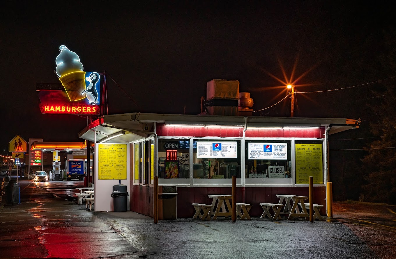 The outside of Eastwind Drive-In at night. There's a neon sign with an ice cream cone lit up with red lettering.