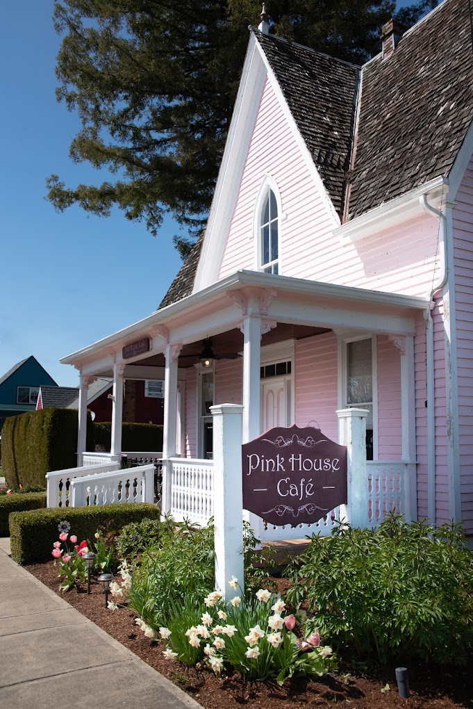 The outside of the Pink House Café. The restaurant is a cute little pink house with white pillars and white porch railing. It has a sharply pitched roof.
