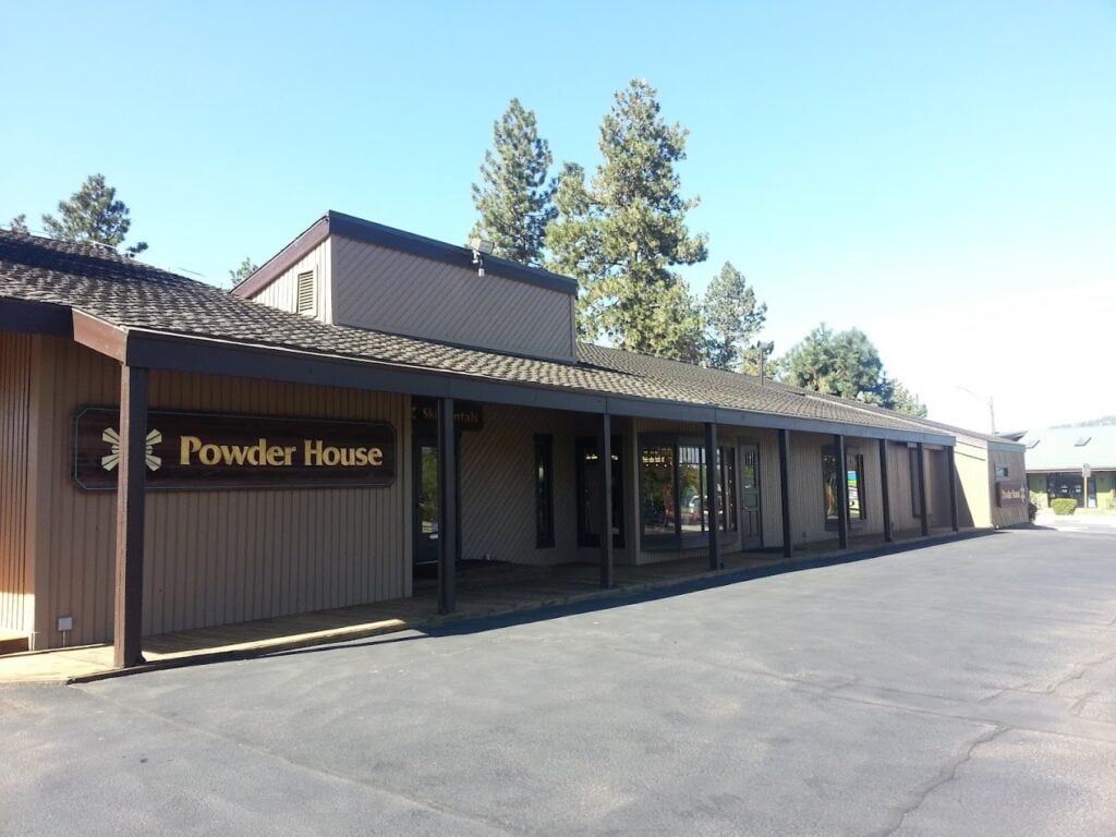 The outside of the Powder House. It's a brown building with tall pine trees behind it on a sunny day with blue skies.