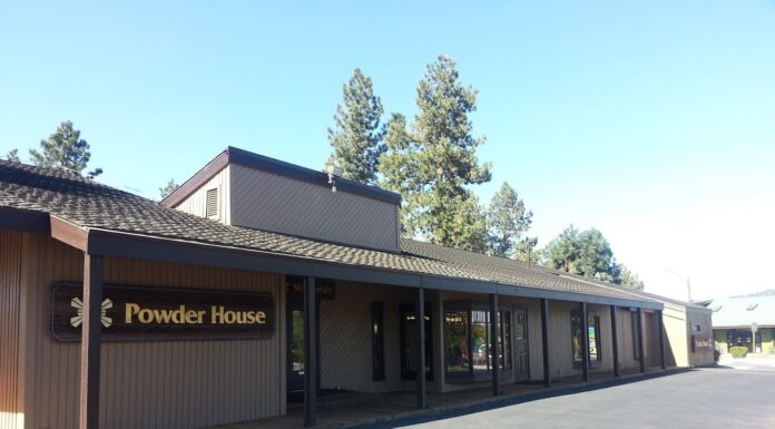 The outside of the Powder House. It's a brown building with tall pine trees behind it on a sunny day with blue skies.