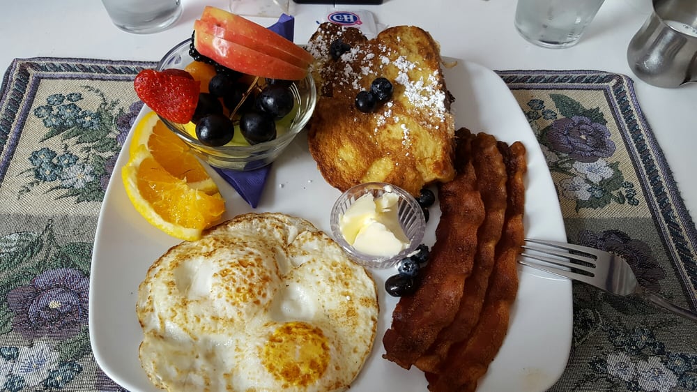Fried eggs, toast, bacon, blueberries and other fruit on a plate. It looks delicious!