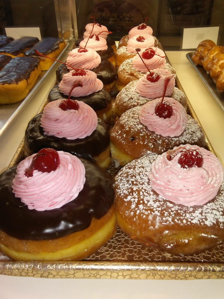 Chocolate donuts and glazed powdered donuts with swirls of pink frosting and a cherry ont op.