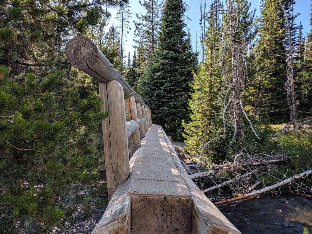 A log going over the creek. There is a railing on one side of the log to make it useful as a bridge.