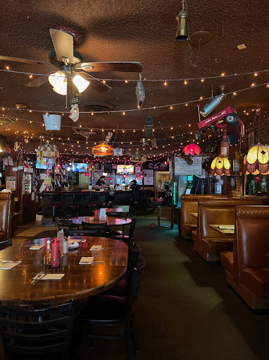 The cozy interior of My Father's Place. In the photo the restaurant and bar are dimly lit, and there are warm string lights strung across the ceiling providing a cozy ambiance.