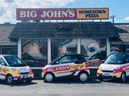 The outside of Big John's Pizza in Pendleton, Oregon. In the photo there are several little white delivery cars for Big John's parked out front.